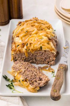 a meatloaf with cheese and onions on a white plate next to a knife