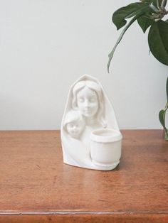 a white statue sitting on top of a wooden table next to a potted plant