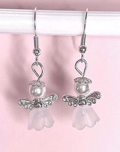 a pair of silver toned earrings with white pearls and angel wings on top of them