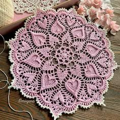 crocheted doily with pink flowers and thread on wooden table top next to it