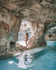 a woman standing in the middle of a pool next to a rock formation with water coming from it