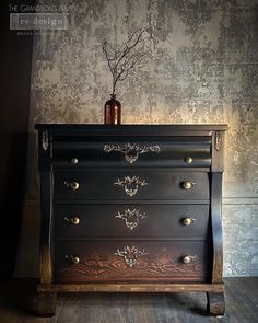 a black dresser with gold accents and a vase on top