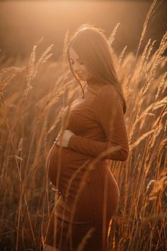 a pregnant woman standing in tall grass at sunset