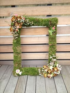 a moss covered letter with flowers and leaves on it sitting in front of a wooden wall