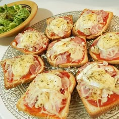 several pieces of bread topped with meat and cheese on a plate next to a salad