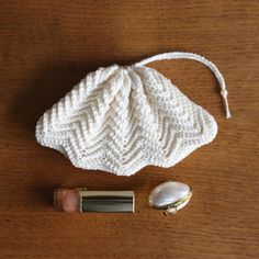 a white purse sitting on top of a wooden table next to a lipstick bottle and a gold case