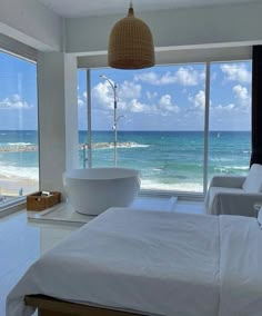 a large white bed sitting next to a window in a bedroom near the ocean with a bathtub