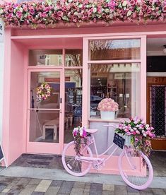 a pink bicycle is parked in front of a storefront with flowers on the windows