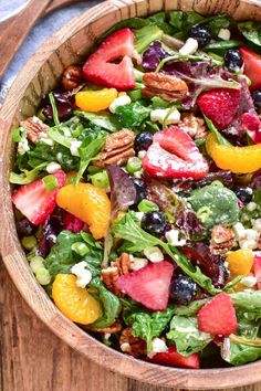 a salad with strawberries, oranges, grapes and pecans in a wooden bowl