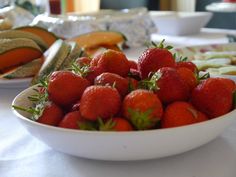 a white bowl filled with strawberries sitting on top of a table next to other plates