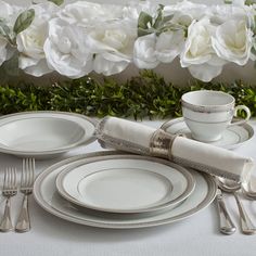 a table setting with white roses in the background and silverware on it, ready to be served