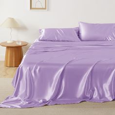 a bed with purple sheets and pillows on top of it, next to a night stand