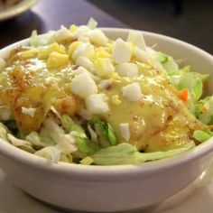 a white bowl filled with salad and dressing on top of a table next to a fork