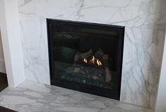 a fire place with a marble fireplace surround and wood burning in the middle, surrounded by white walls