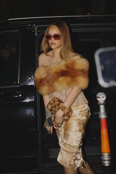 a woman in a gold dress and fur stoler walking out of a black car