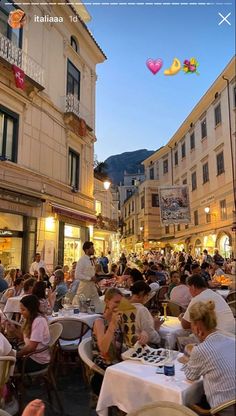 many people are sitting at tables outside in the evening, with balloons flying above them