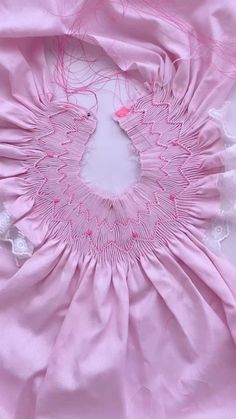 a close up of a pink dress on a white surface with red thread and lace