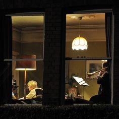 two people are sitting in a window playing instruments at night, one person is looking out the window