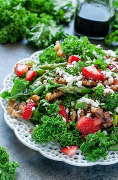 a salad with strawberries, nuts and greens on a white plate next to a bottle of wine