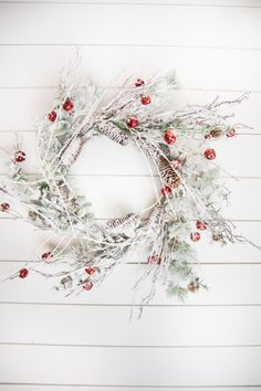 a white wreath with pine cones and red berries