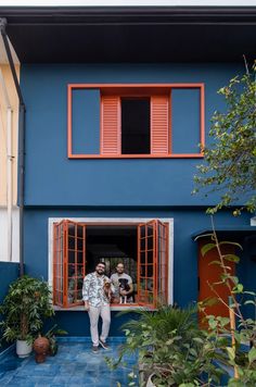 two people are standing in the open door of a blue and orange house with red shutters