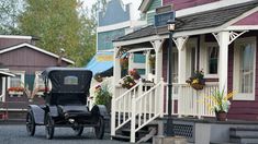 an old fashioned car is parked in front of some small wooden houses with flowers on them