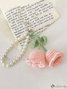 two crocheted baby booties are next to a pearl necklace and book page