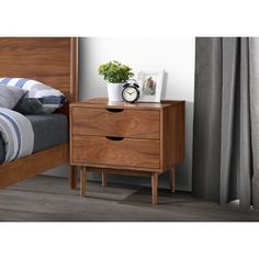 a nightstand with two drawers and a clock on it next to a bed in a bedroom