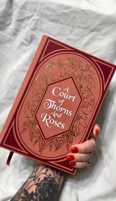 a woman is holding a book with writing on the front and back cover that reads court of thins and roses