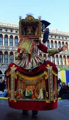 a man in costume walking down the street with an elaborately decorated cart behind him