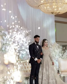 a man and woman in formal wear standing next to each other near a chandelier