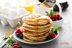 a stack of pancakes with syrup being drizzled over them and topped with berries