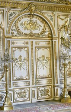 an ornate gold and white room with chandeliers on either side of the door