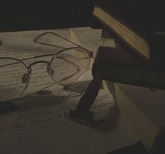 a pair of glasses sitting on top of an open book next to a pen and eyeglasses