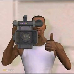 a man is holding a camera and giving the thumbs up while wearing a white tank top