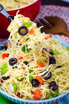 a spoonful of pasta with olives and peppers is being lifted from a bowl