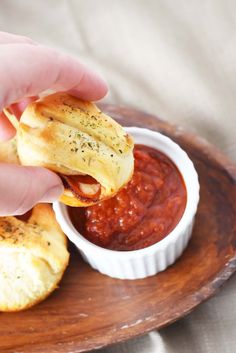 a person is dipping some food in a small bowl on a wooden plate with sauce