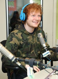 a young man with headphones on sitting in front of a microphone and smiling at the camera