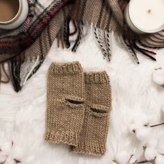 a pair of knitted mittens sitting on top of a white blanket next to a cup of coffee