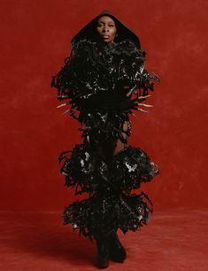 a woman in a black dress with feathers on her body and hood over her head