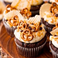 several cupcakes with chocolate frosting and pretzels on top sitting on a wooden platter