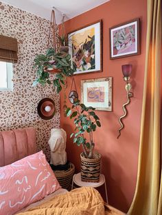 a bedroom with orange walls and pictures on the wall above the bed, along with a potted plant