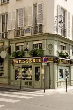 the corner of a street in front of a tall building with windows and shutters