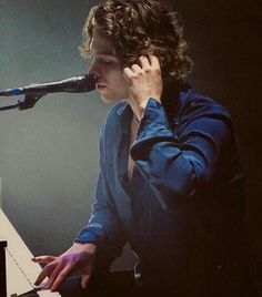 a man sitting in front of a microphone while playing a piano with his hands on the keyboard