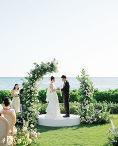 a couple getting married in front of an arch with flowers and greenery on it