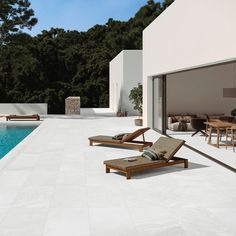 two lounge chairs sitting on top of a white tiled floor next to a swimming pool