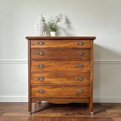 a wooden dresser with two vases on top of it next to a white wall