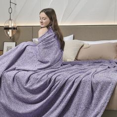 a woman wrapped in a purple blanket sitting on a bed