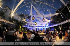 a group of people sitting around tables under a tent with lights on it at night