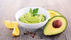 an avocado in a white bowl next to sliced lemons on a wooden table